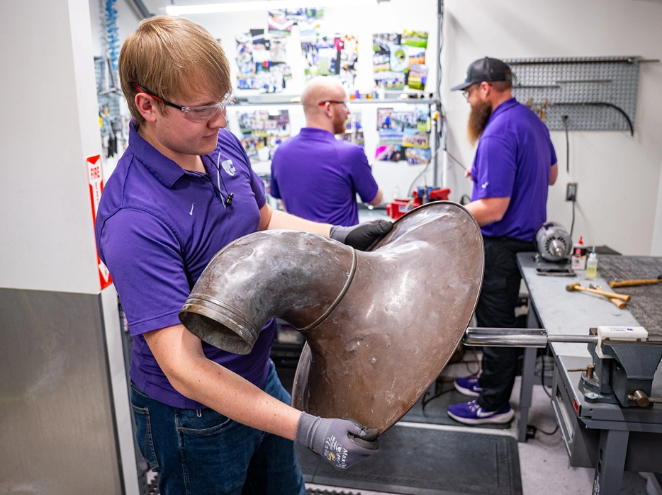 Chase Wassom rolls out the dents on the bell of the horn he is restoring. The steel tool requires finesse — a ball bearing rolls around and helps shape and knead out dents in an instrument's metal. (Photo courtesy K-State University News and Communications)