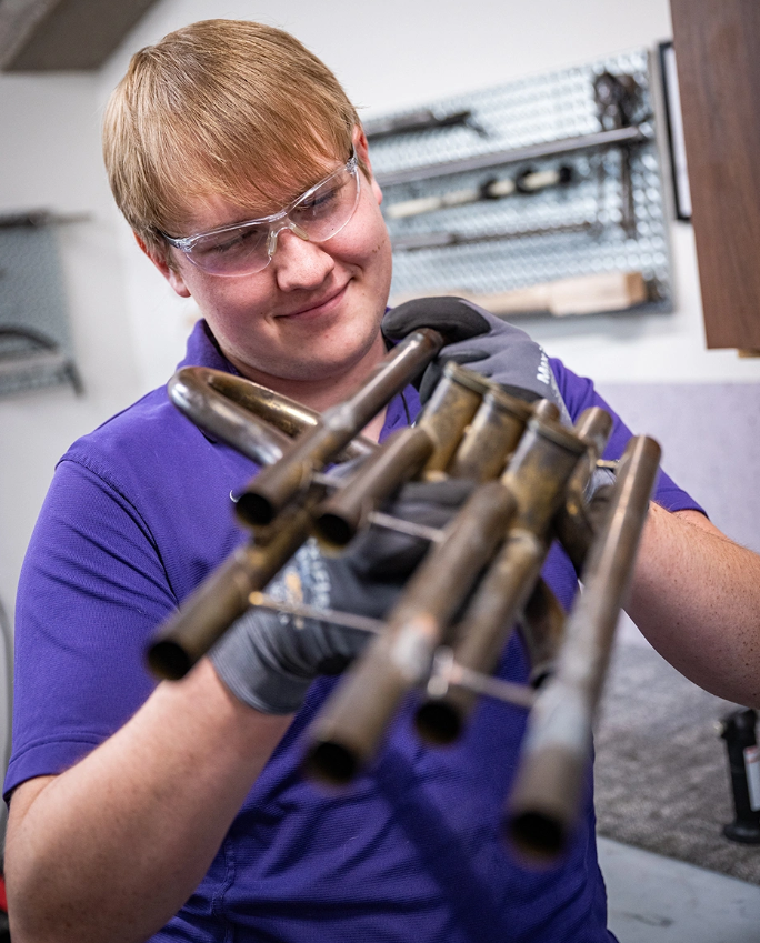 Chase Wassom examines a brace he had made and how it aligns on the valve block of the horn he's restoring. (Photo courtesy K-State News and Communications)