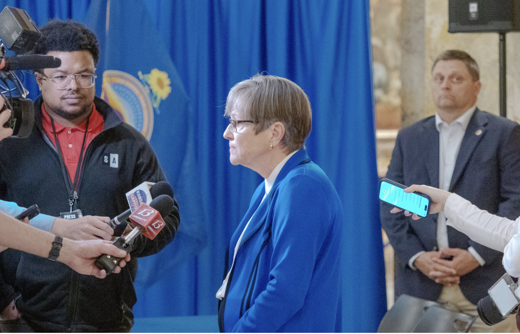  Gov. Laura Kelly, seen talking to reporters March 31, 2026, at the Statehouse, says the Legislature should stay out of women’s private medical decisions. She vetoed a pair of anti-abortion bills that compel doctors to spread misinformation to patients and make it easier for women to sue abortion providers. Republicans are expected to override the Democratic governor’s vetoes. (Photo by Sherman Smith/Kansas Reflector)