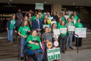 Advocates for medical cannabis join together before a public hearing at the Nebraska State Office Building in Lincoln, Nebraska, on state-drafted regulations for the new medicine approved by Nebraska voters in November 2024. Front left is Tiffany Tex Gustafson. Oct. 15, 2025. (Zach Wendling/Nebraska Examiner)