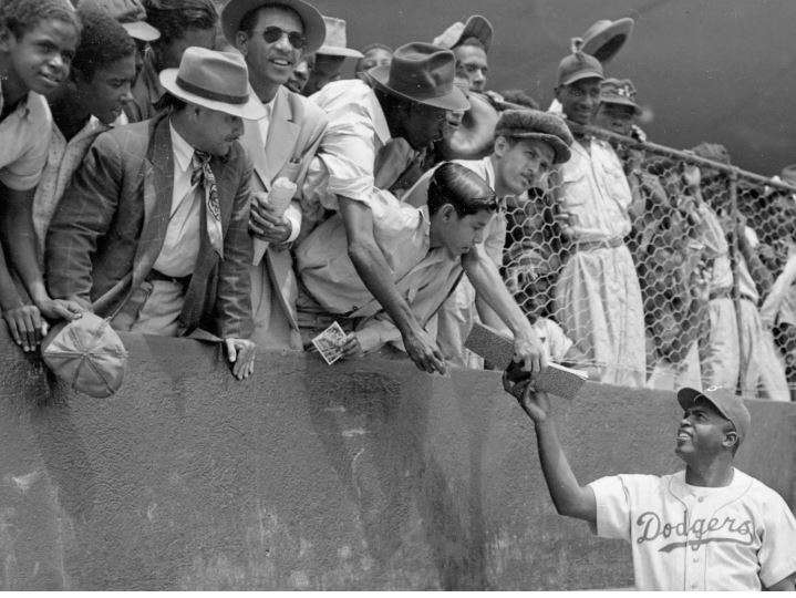 FILE - Jackie Robinson, first baseman of the Brooklyn Dodgers, returns an autograph book to a fan in the stands, during the Dodgers' spring training in Ciudad Trujillo, now Santo Domingo, in the Dominican Republic, on March 6, 1948. (AP Photo/File)
