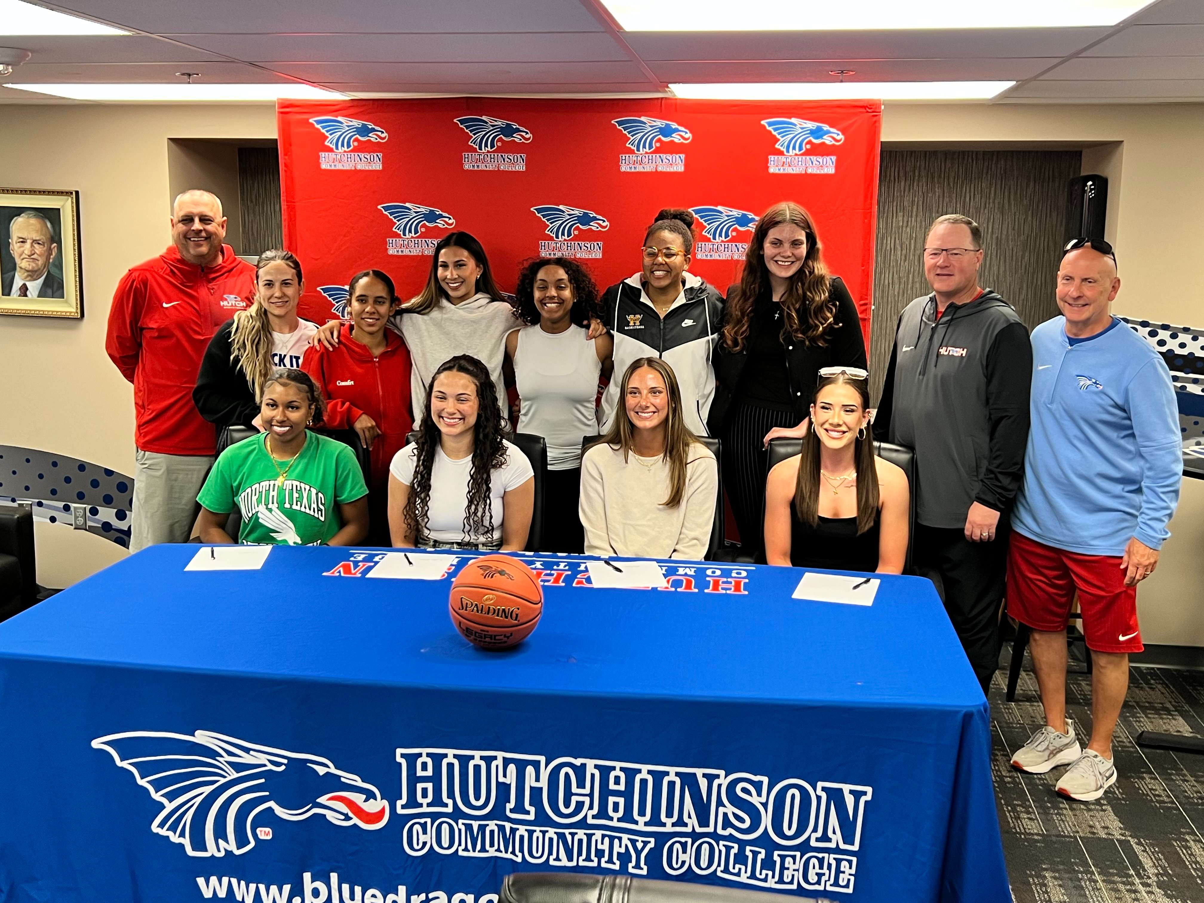 Hutchinson Community College women’s basketball players KaMyra Barber, Jaden Wilson, Noelle Anthon and Katie Duncan are joined by members of the 2025-26 Blue Dragon women’s basketball team and coaching staff Wednesday after signing National Letters of Intent in the Club 1928 Room at the Hutchinson Sports Arena. (Hutch Post Photo/Sean Boston)
