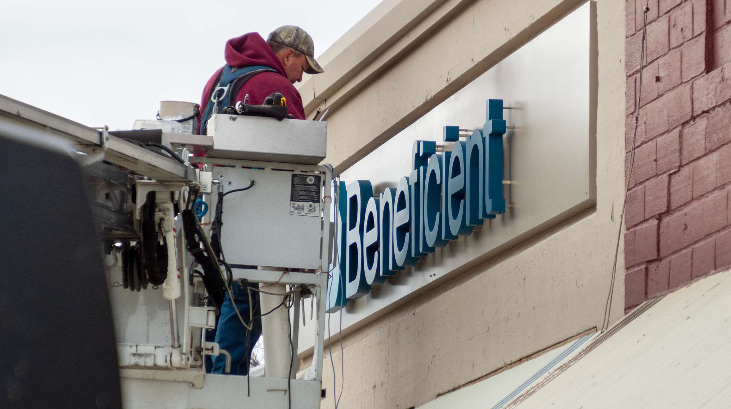 Ray Katzer, of Luminous Neon, paints the Beneficient name onto the company’s office building in April 2022 in downtown Hesston. (Photo by Sherman Smith/Kansas Reflector)
