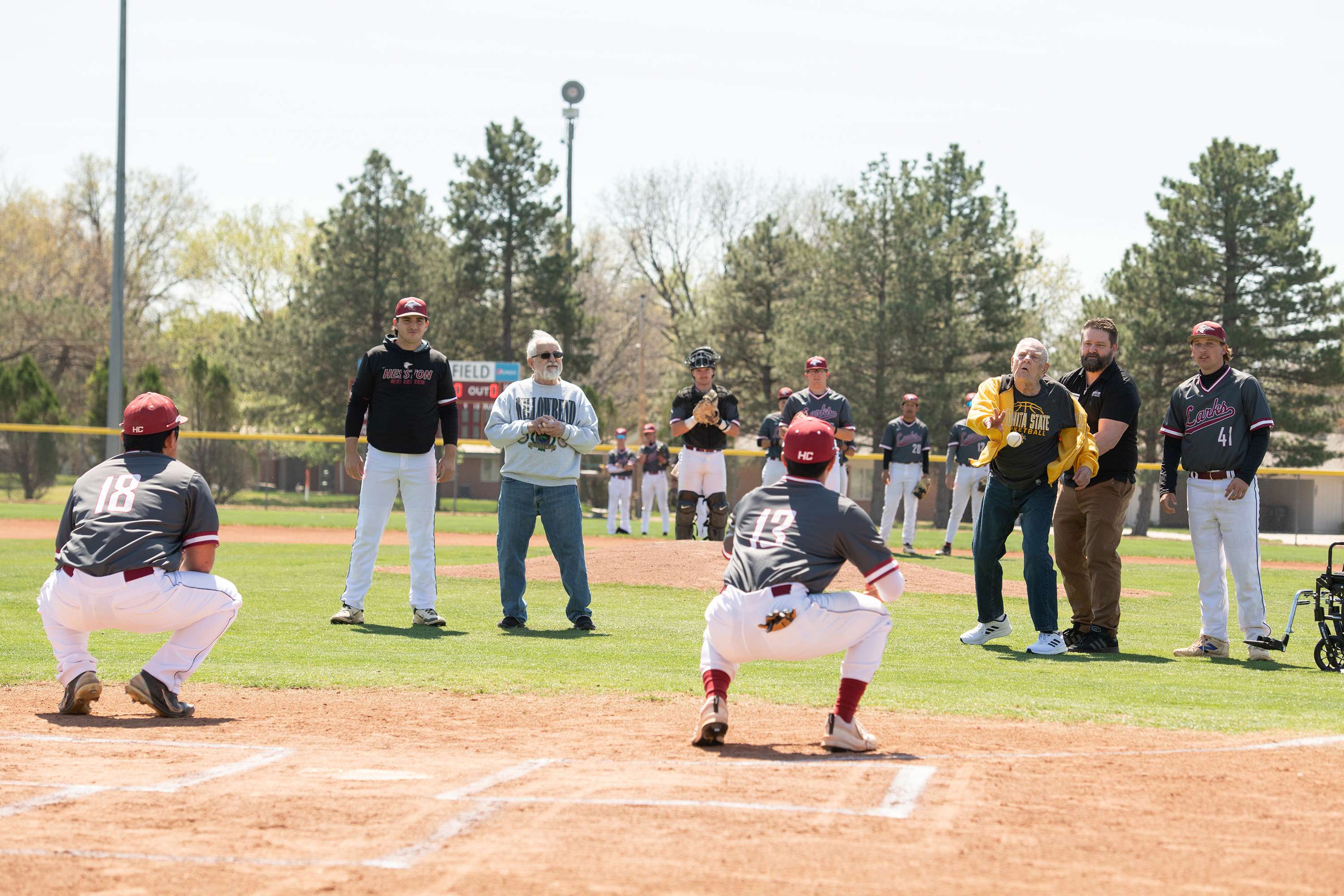 Schowalter Villa residents James Thomas, left, and JB Ensz, right, throw out a ceremonial first pitch at the Hesston College baseball game. Photo by Larry Bartel, Hesston College.