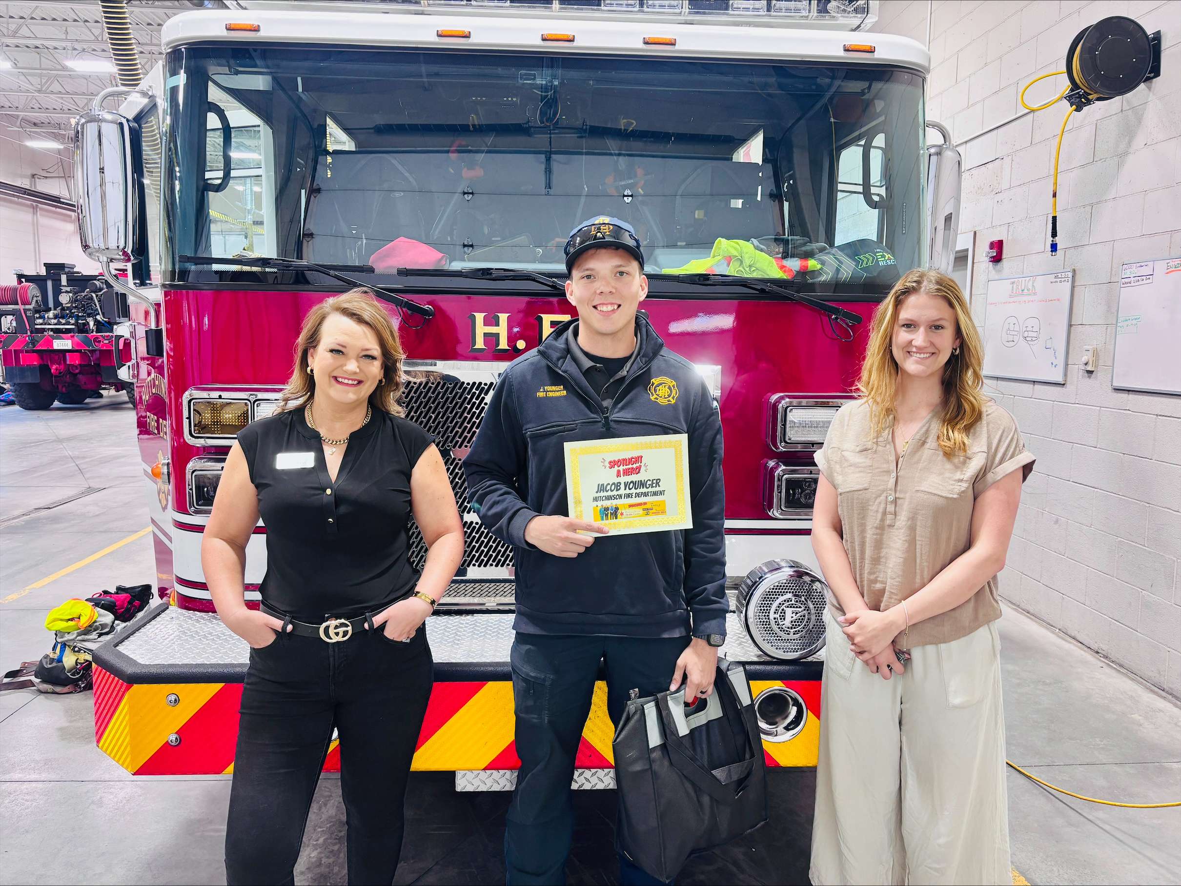 Eagle Media Digital Marketing Manager, Ashley Weve, left, Hutchinson Fire Department firefighter Jacob Younger, center, and PrairieStar Health Center Director of Marketing, Kyran Losew, pose in front of a fire engine, after Younger was named the First Responder of the Month for May. The honor is sponsored by PrairieStar Health Center and Eagle Media. Younger also received a gift bag from Smith’s Market. (Hutch Post photo)