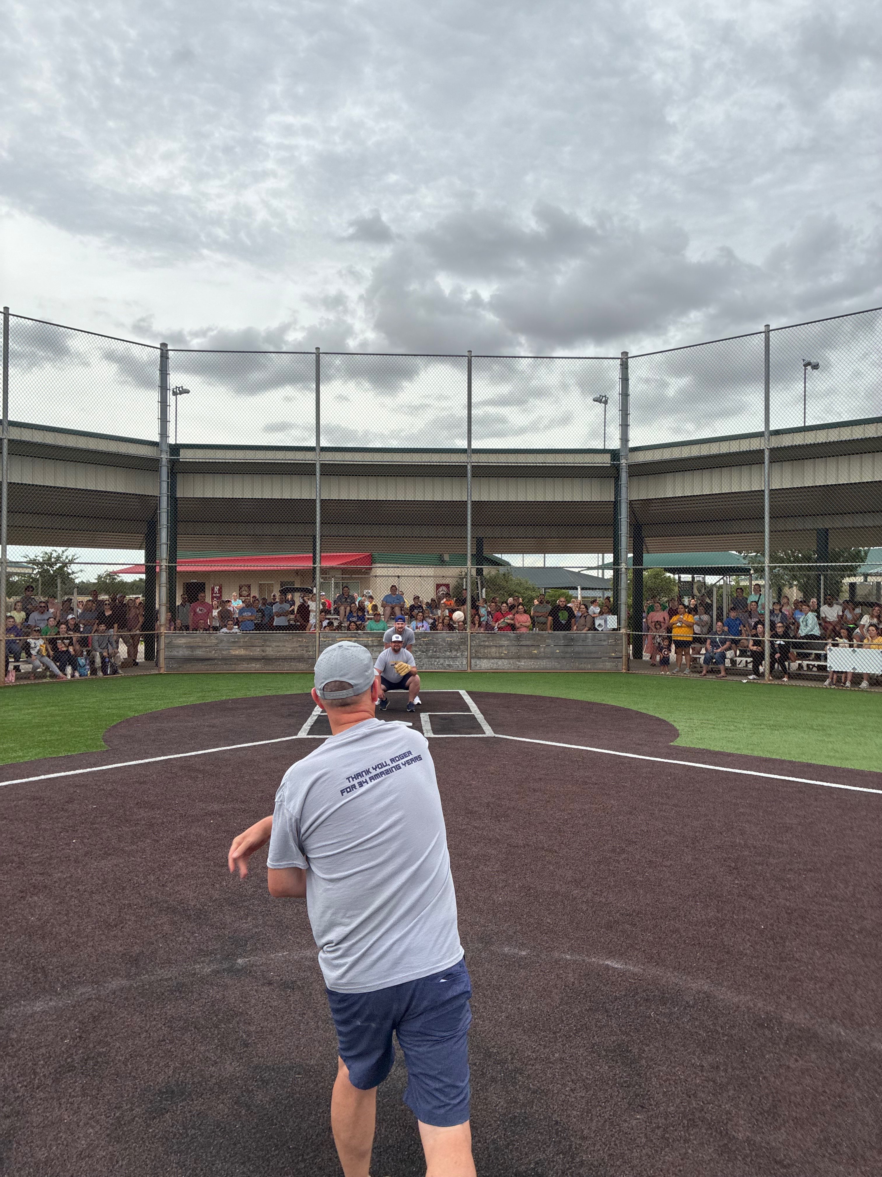 Roger Bixenman throwing the ceremonial first pitch of the 2026 season to his son Shane Bixenman while his other son Derek Bixenman acts as the umpire. Photo by Alin Hett/Hays Post