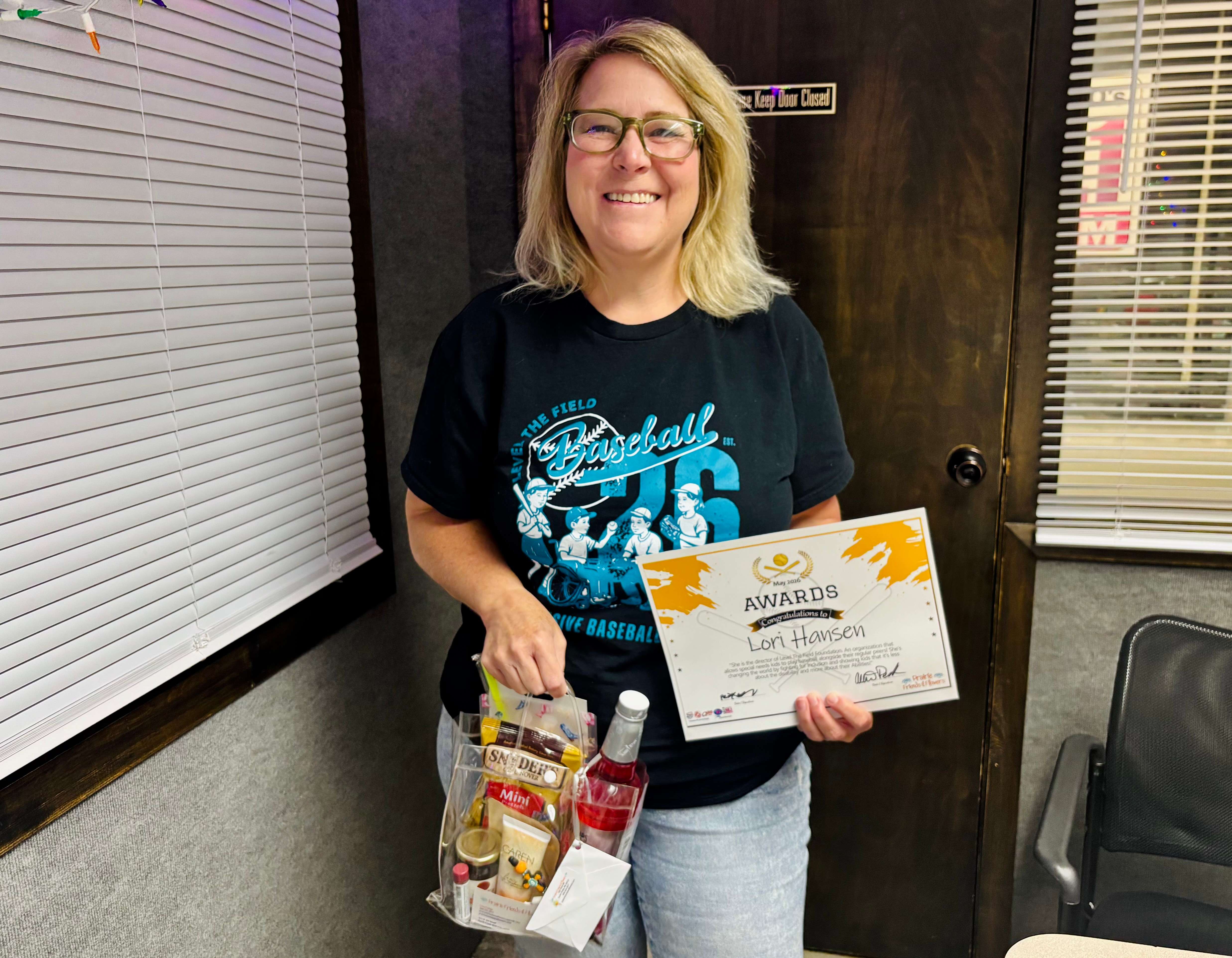 Lori Hansen smiles with her Community Hero for Kids award and gift basket from Prairie Friends and Flowers. Hansen was recognized for her dedication to expanding adaptive sports and activities for children with disabilities through the Level the Field Foundation.