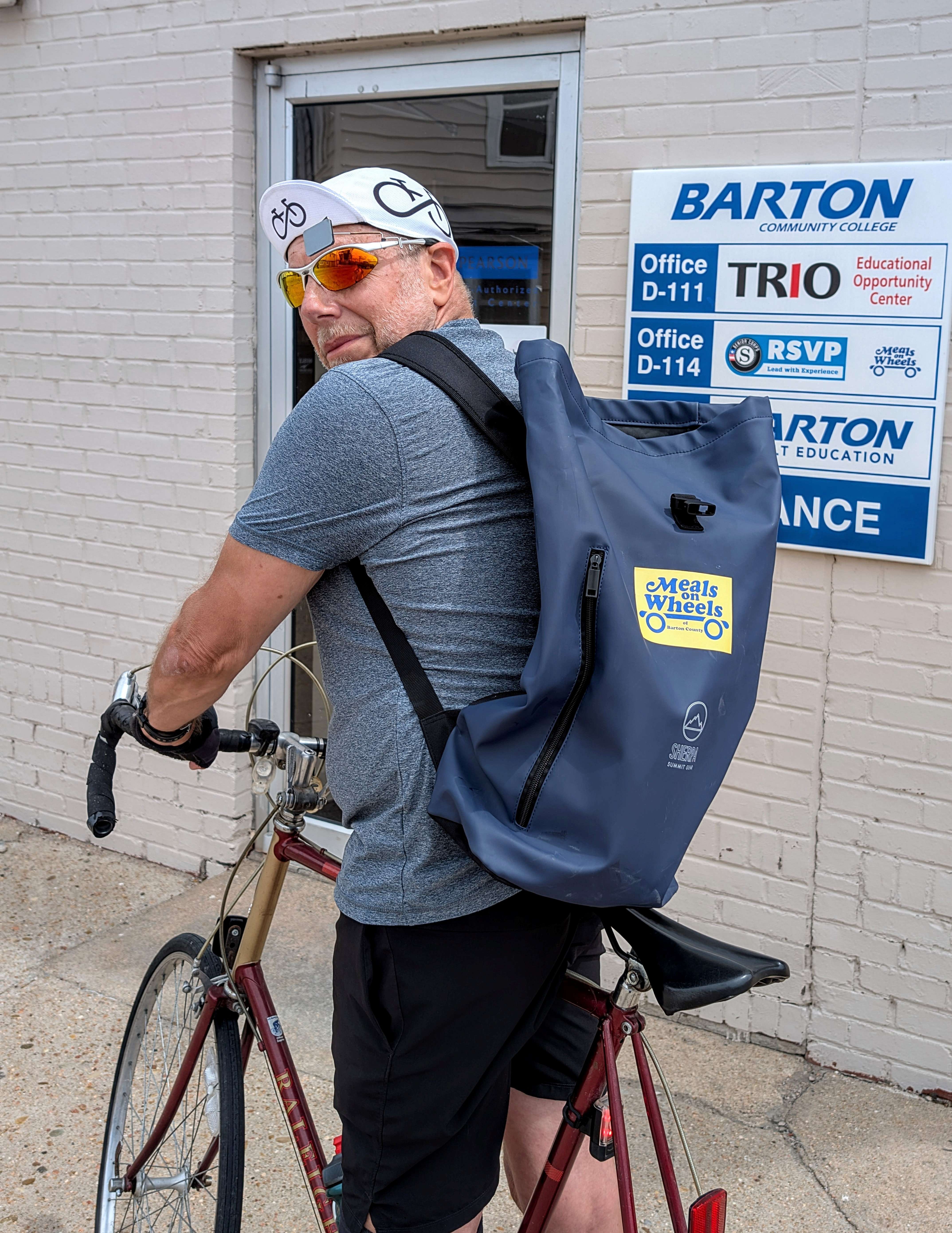 Meals on Wheels of Barton County volunteer Dale Hogg demonstrates how he delivers the meals on his route by bicycle.