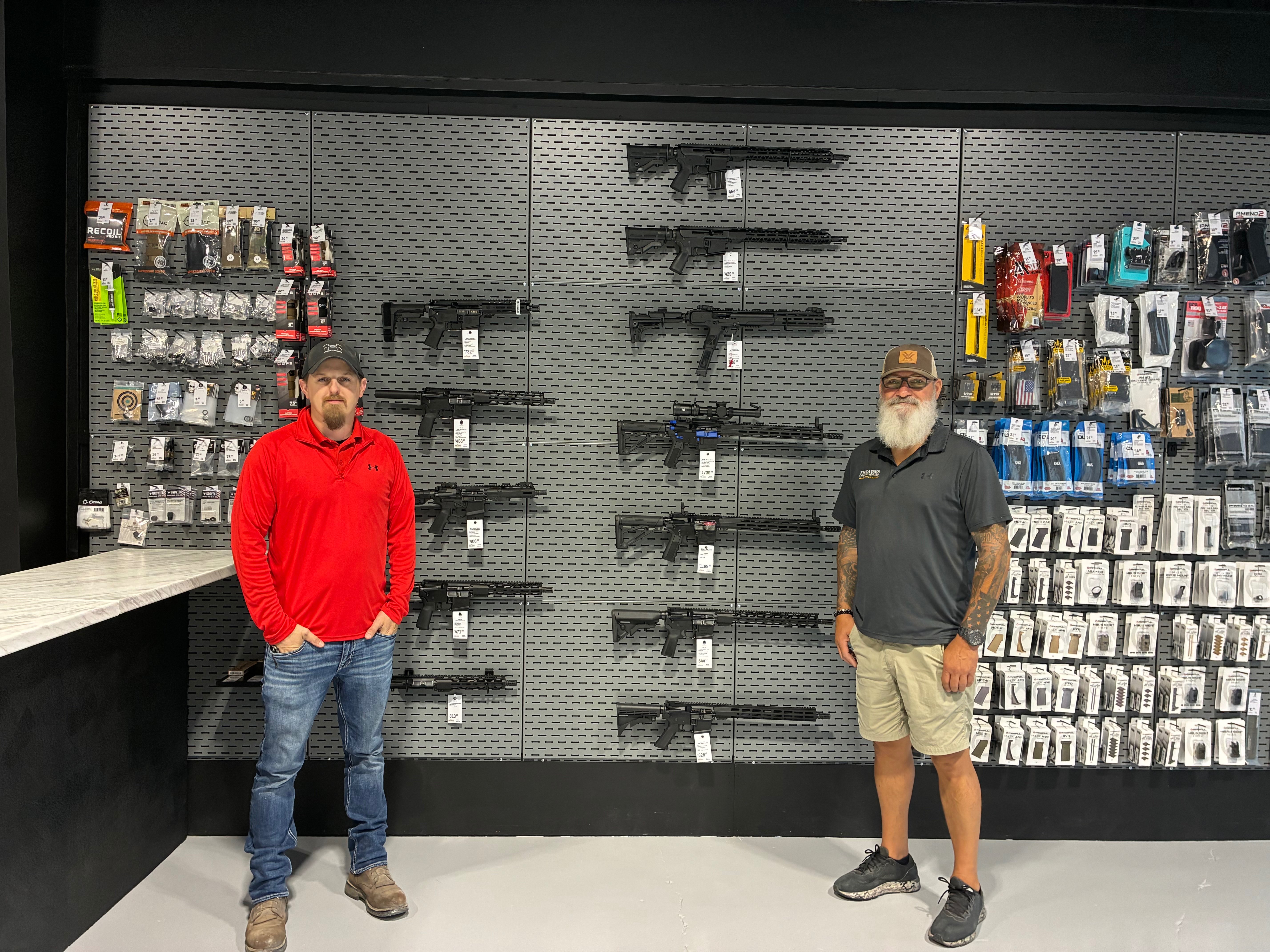 Co-owner Richard Hodges, left, and employee Justin Richardson, right, stand in front of FASARMS' collection of high-powered rifles at the company's new location at 1240 Vine St. in Hays. Photo by Alin Hett/Hays Post. <br>