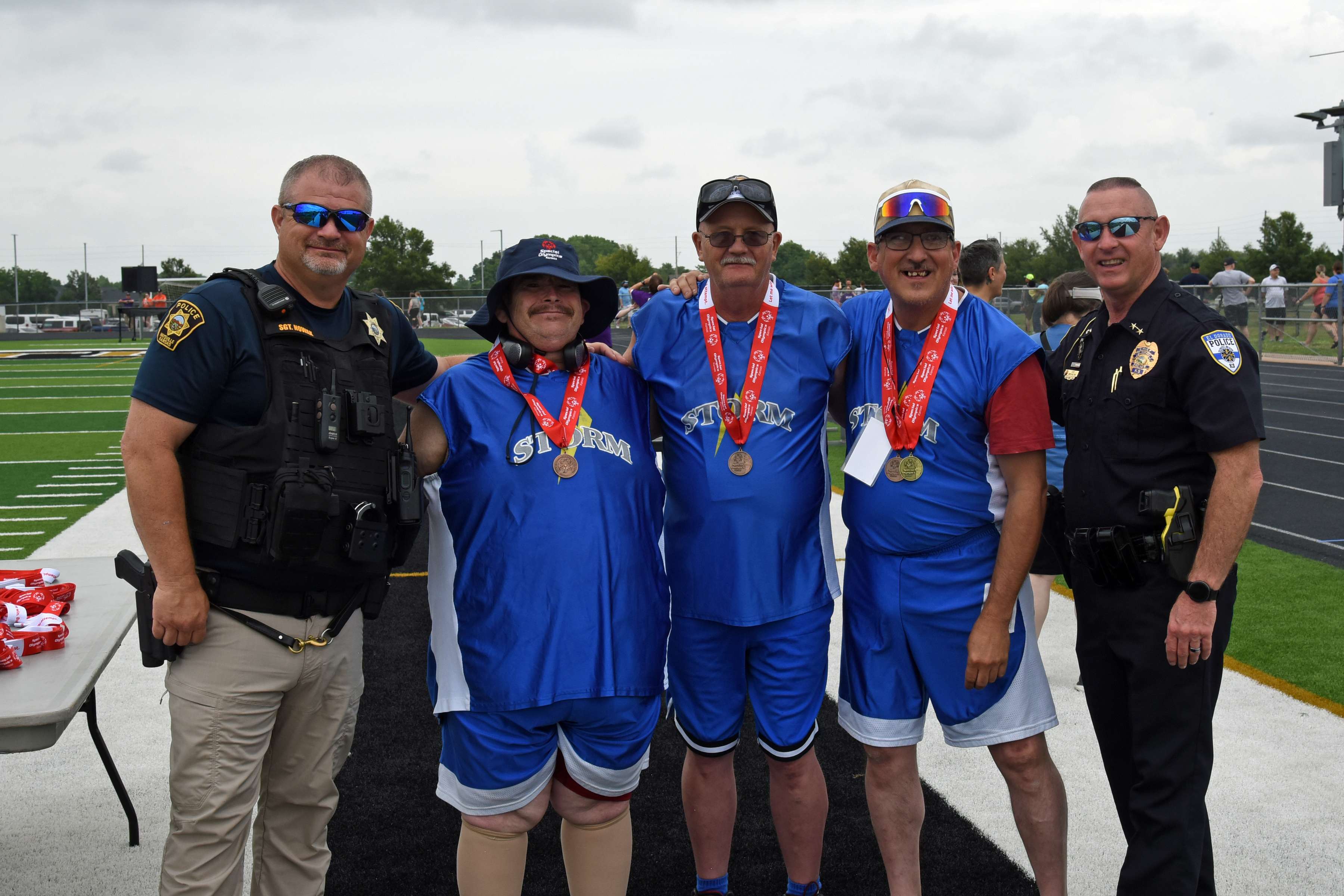 Storm track and field athletes (left to right) Chris Devine, Steve Smolik, and Michael Manka take a photograph with Wichita Law Enforcement following the 50-meter race walk at the State Track Championships at Maize South High School on June 6.