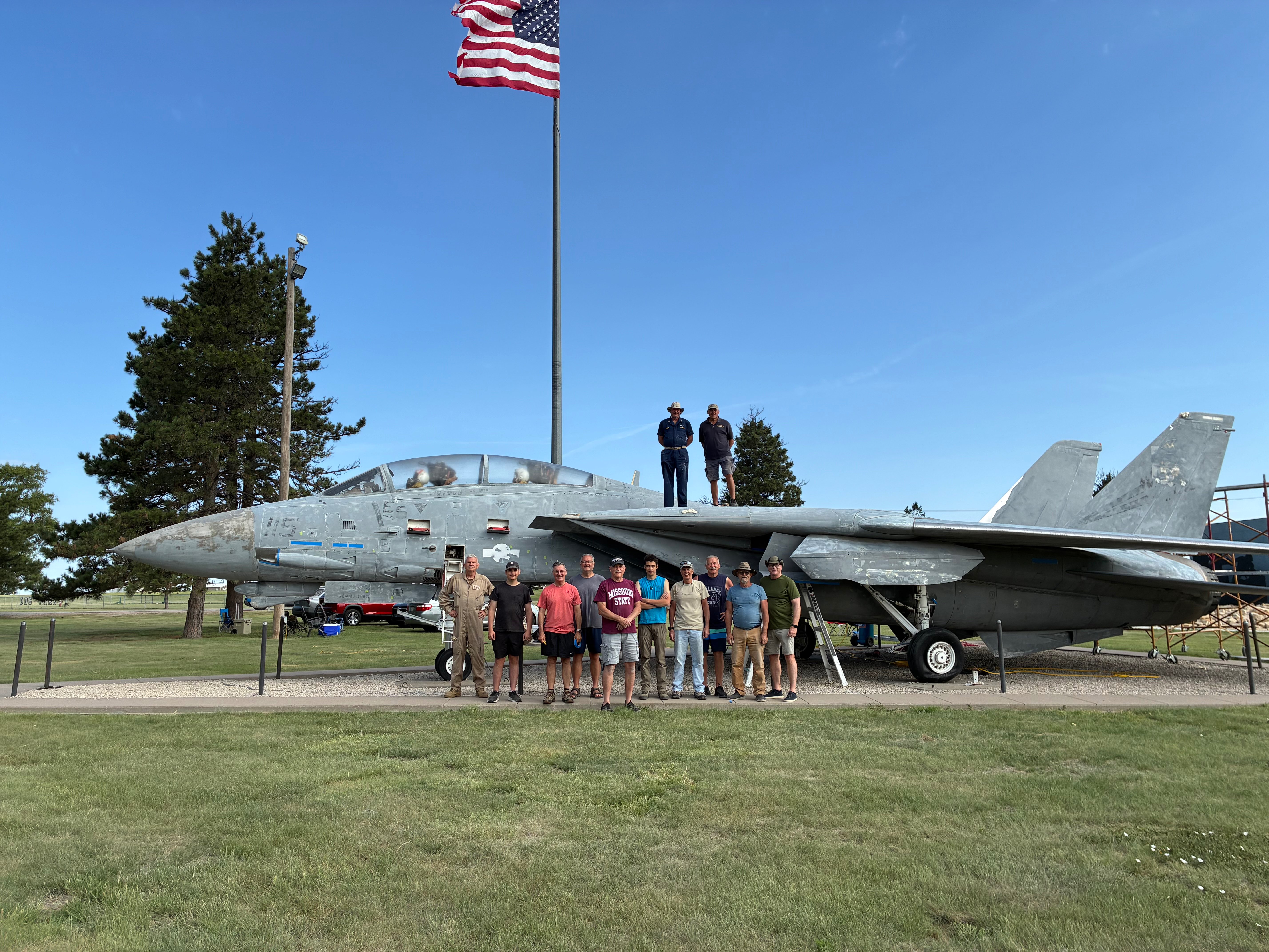 Members of the F-14 Tomcat Association pose in front of the F-14 Tomcat they are restoring. From left: Martin Byfield, Hays native and Utilities First Class; Sam Bruce, 17-year-old volunteer; Randy Addison, Commander, U.S. Navy, callsign “Cracker”; Steve Bruce, Navy avionics technician; Rear Admiral Hamlin Tallent, U.S. Navy, callsign “Ham”; Benedict Stuart, volunteer; Gary Williams, Captain, U.S. Navy, callsign “Grip”; Don Sloane, Lieutenant Commander, U.S. Navy, callsign “Pappy,” also served as a radar intercept officer; Michael Martin, AT1 aviation electronics technician, callsign “Magic”; and James Walker, Lieutenant and RIO, U.S. Navy, callsign “JJ.” Standing on top of the aircraft are Pat Ritchie, aviation structural mechanic chief petty officer, callsign “Richy Rich,” and Ben Mostowy, aviation electronics technician second class petty officer. Photo by Alin Hett/Hays Post.&nbsp;<br>