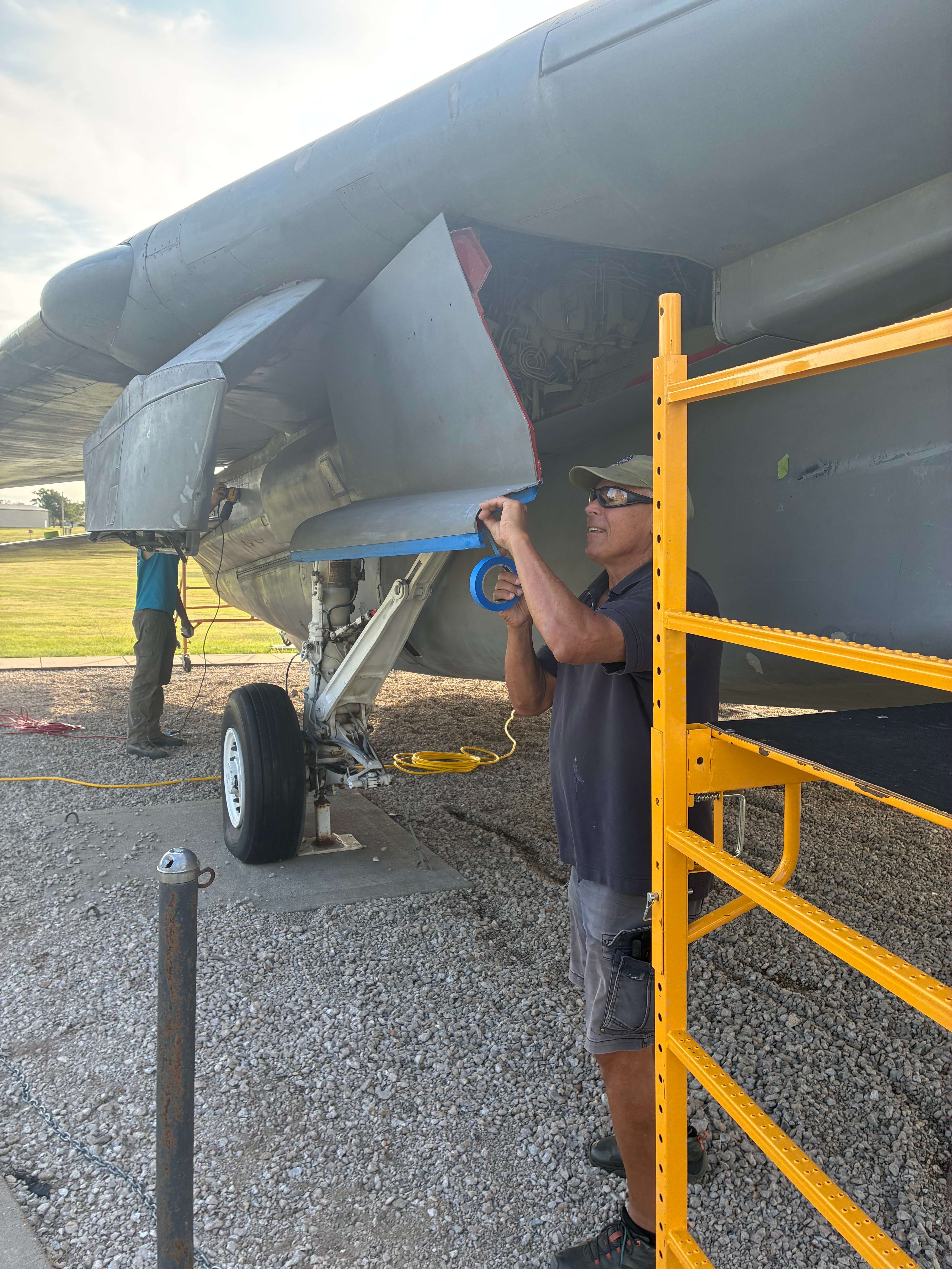 Ben Mostowy, aviation electronics technician, second class petty officer, putting tape over the bottom of the wing as the F14 Tomcat Association gets ready to repaint the fighter jet. Photo by Alin Hett/Hays Post