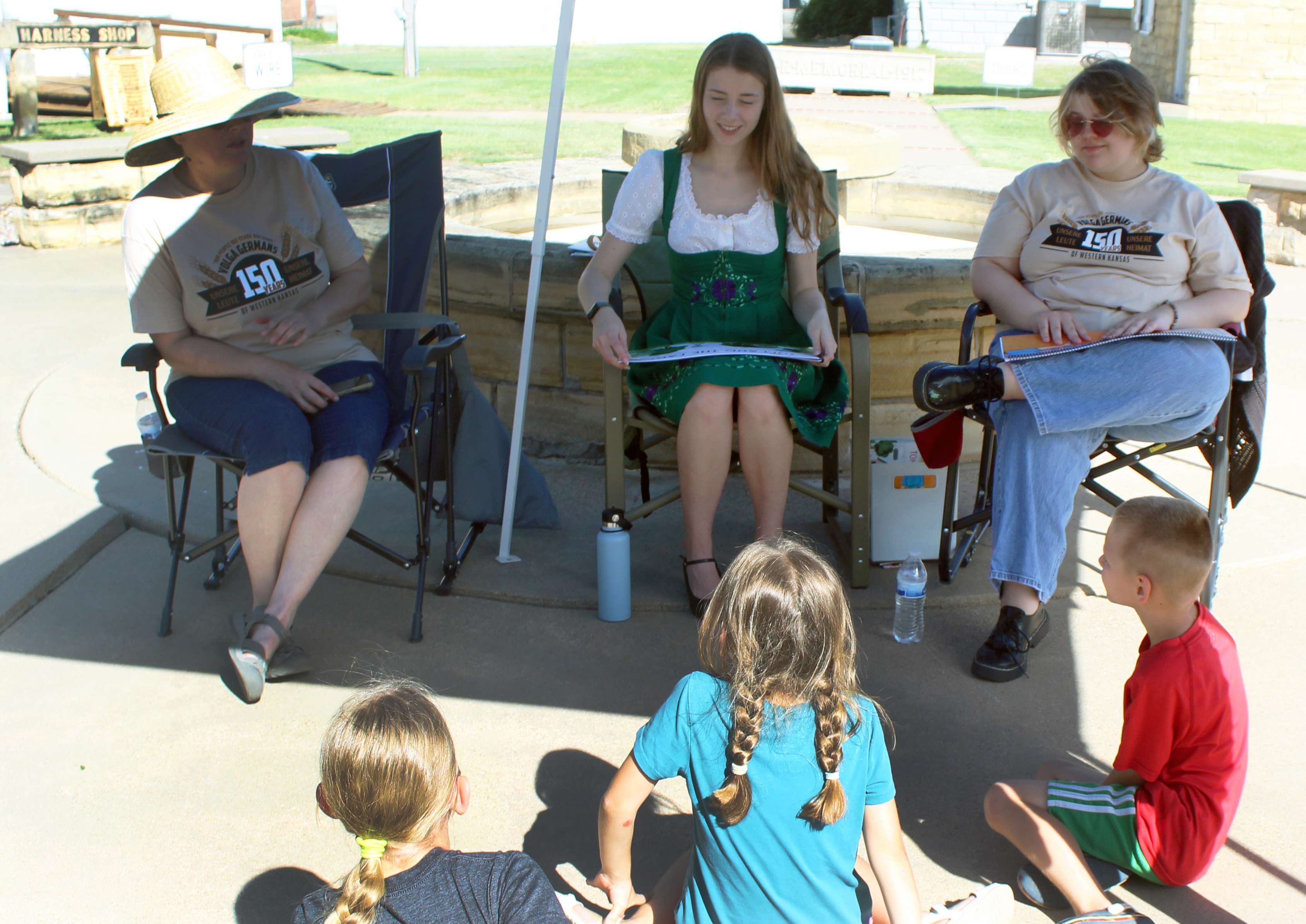 Mariella&nbsp;Dreiling, Hays High graduate, reads&nbsp;"Tom and the Farm," which she wrote, to a group of children June 13 at Kinderfest at the Ellis County Historical Museum. Willow Nickell, Hays High graduate, right, illustrated the book. Codi Fenwick, left, was the girls' Hays High teacher. Photo by Cristina Janney/Hays Post