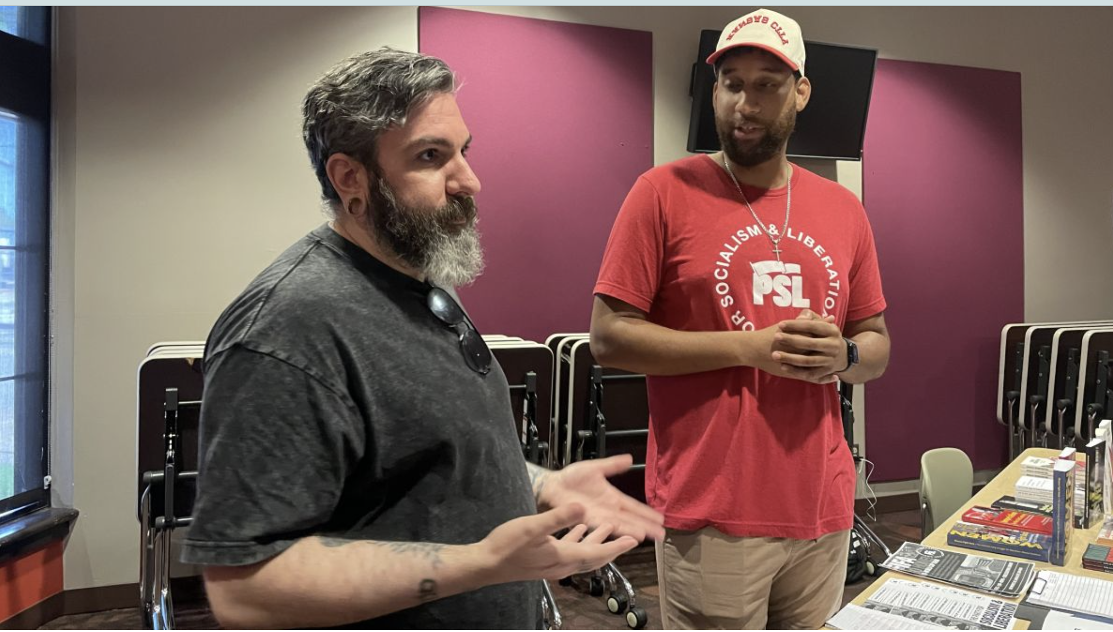  Lyon Lenk (left) and Nate Davis talk with attendees during a recent meeting of the Party for Socialism and Liberation. The group received updates on the Monarch Pledge and other efforts to highlight worker and immigrant rights during the FIFA World Cup 2026 (Mary Sanchez/The Beacon).