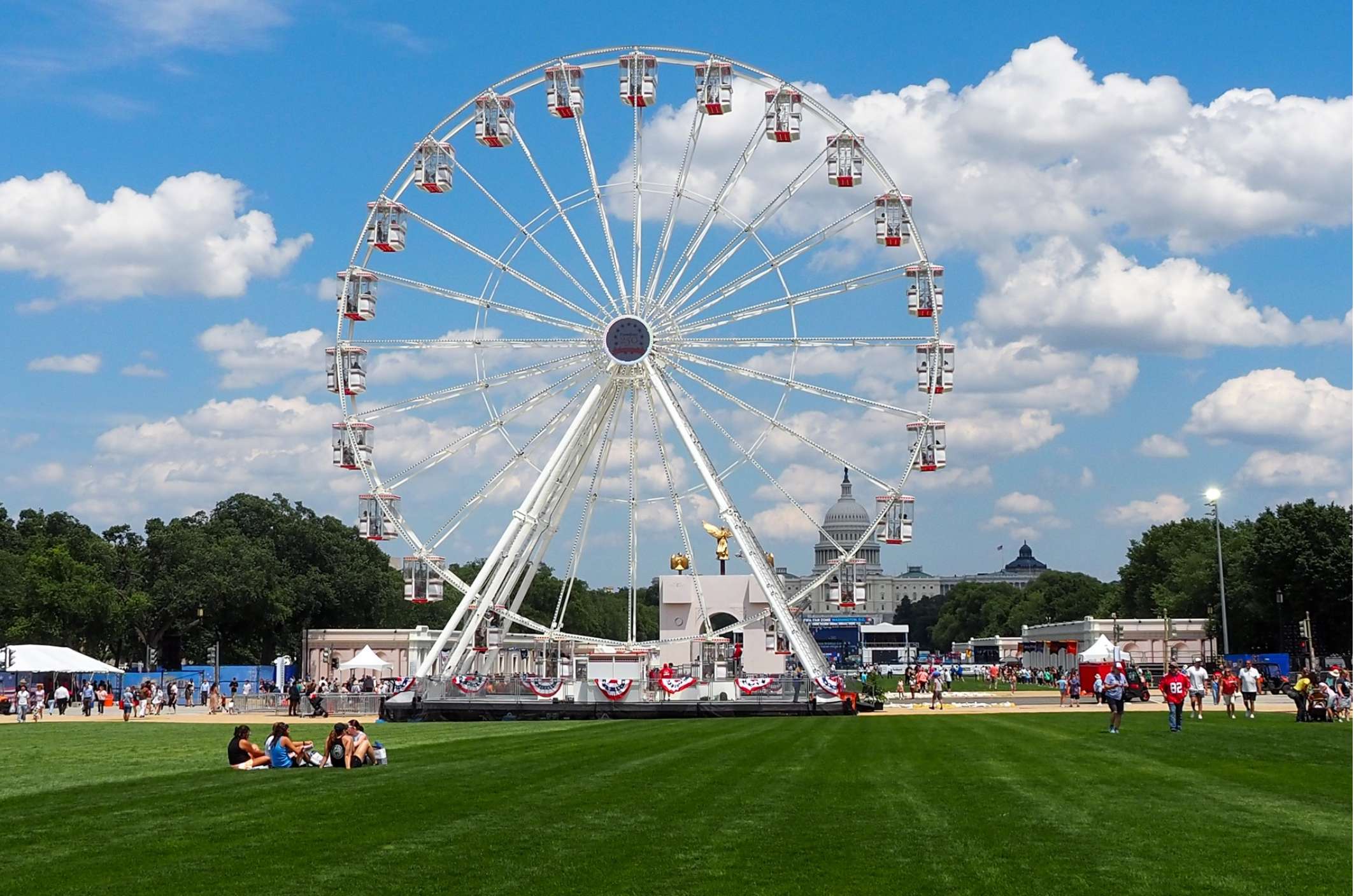  Attendees sit in the grass in front of the Ferris wheel at the Trump administration’s Freedom 250 Great American State Fair on the National Mall on Thursday, June 25, 2026. (Photo by Ashley Murray/States Newsroom)