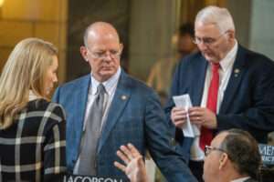 State Sens. Christy Armendariz of Omaha, left, Paul Strommen of Sidney, center and Mike Jacobson of North Platte meet on the floor of the Nebraska Legislature. Jan. 29, 2026. (Zach Wendling/Nebraska Examiner)