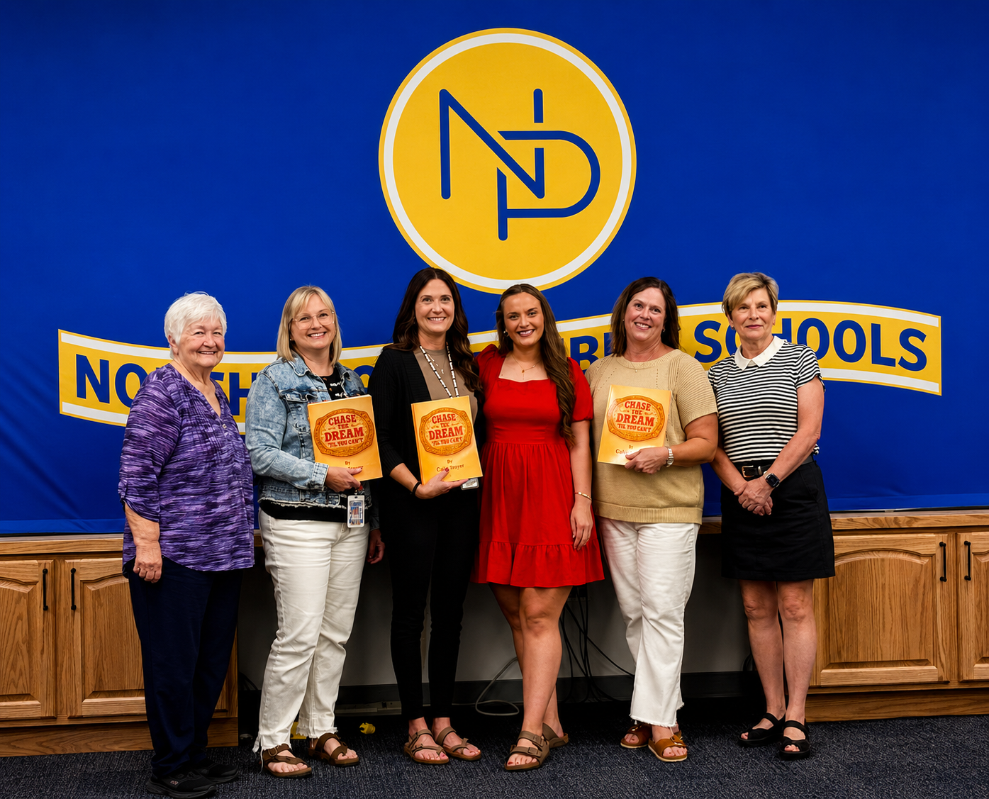 Calie Troyer (center, red dress) is joined by North Platte Public Schools media specialists and representatives of PEO Chapter EB after donating copies of her children's book, Chase the Dream 'Til You Can't, to every North Platte Public Schools elementary library. Marilyn McGahan, president of PEO Chapter EB, is pictured at far left. (Allison Peck | The Post)