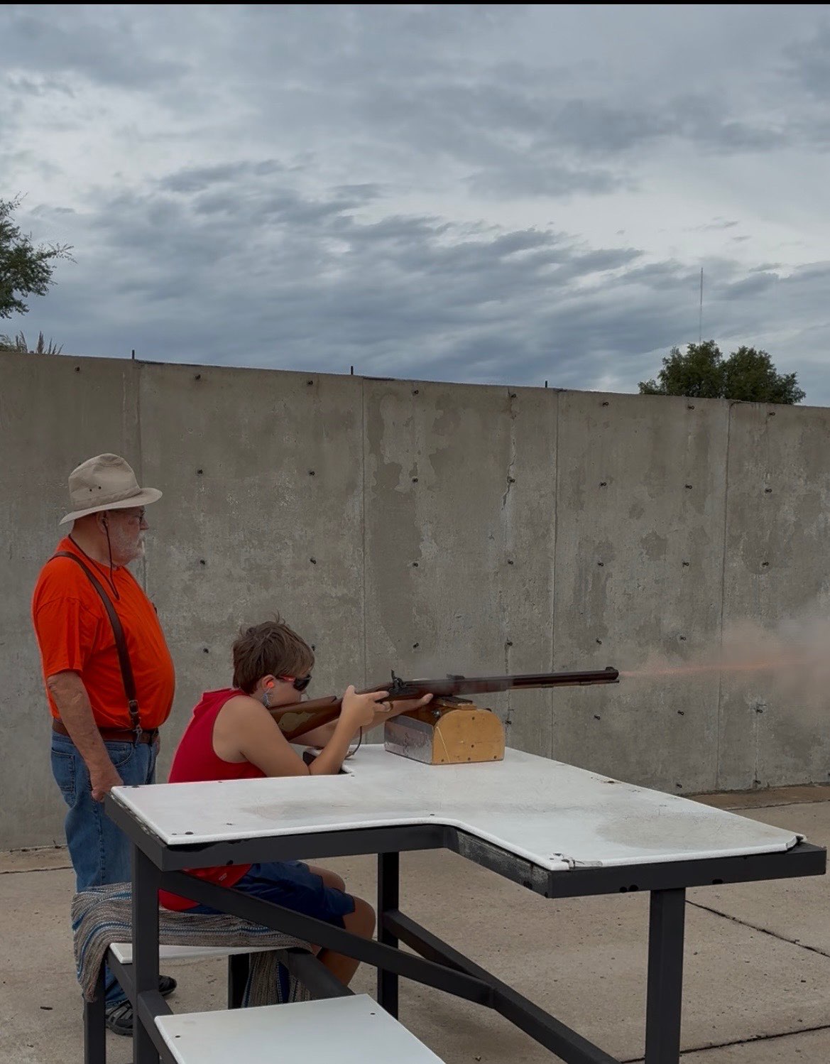 Bentley Frazier fires a rifle, with the bullet visible leaving the barrel, as Gerald Thyfault supervises during a shooting activity at the 29th annual Youth Outdoor Festival. Photo by Alin Hett/Hays Post<br>