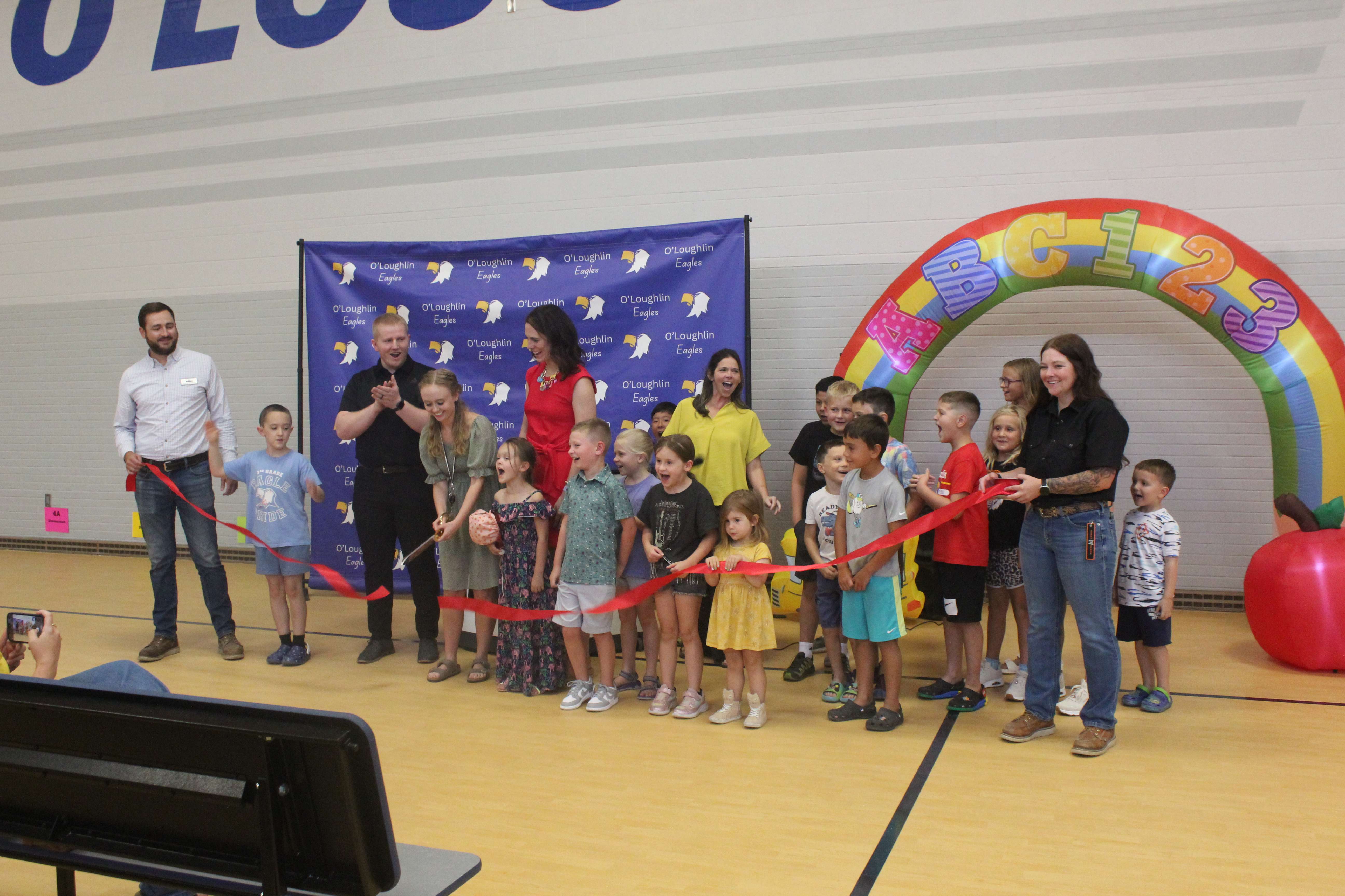 Children, new O'Loughlin Elementary School teachers, Principal Renee Burns and a representative of Nabholz Construction cut the ribbon on the additions and renovations at the school on Wednesday night. Photo by Cristina Janney/Hays Post