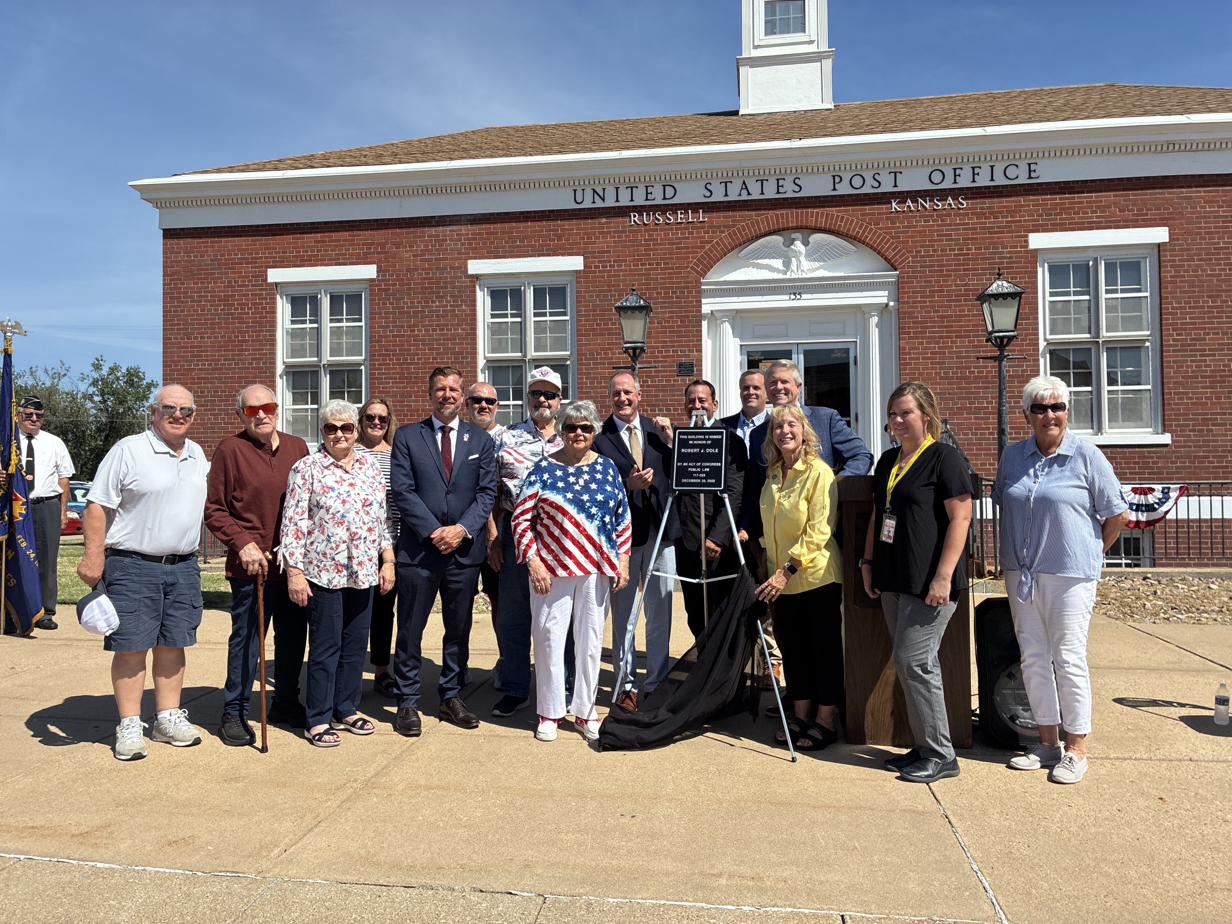 Family members, members of Congress, Bob Dole Post Office staff and those close to Dole gather around the plaque bearing the words, "This building is named in honor of Robert J. Dole." Photos by Alin Hett/Hays Post
