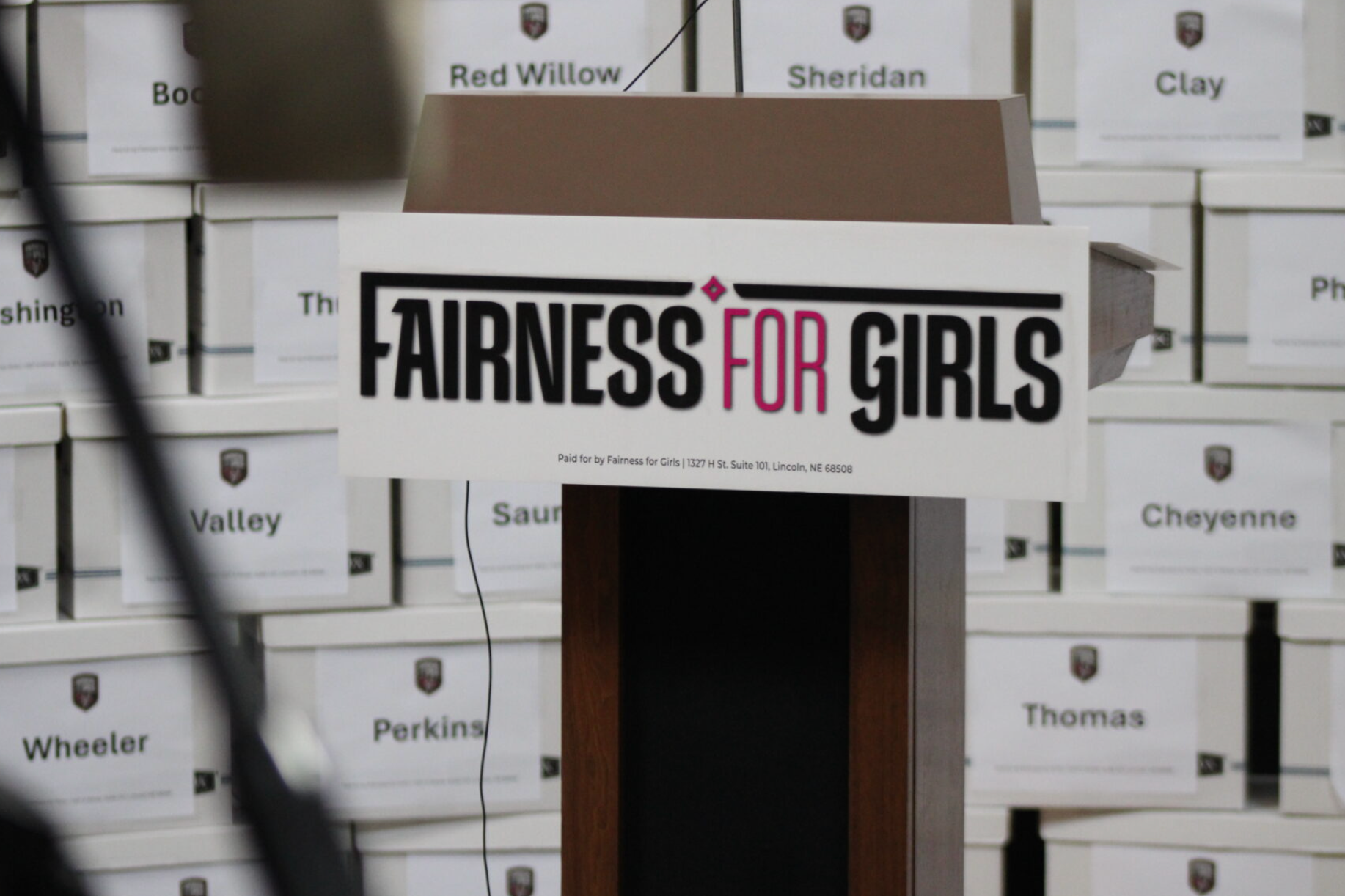 the group “Fairness for Girls” sign on a podium in Lincoln on June 30, 2026. (Juan Salinas II/Nebraska Examiner)