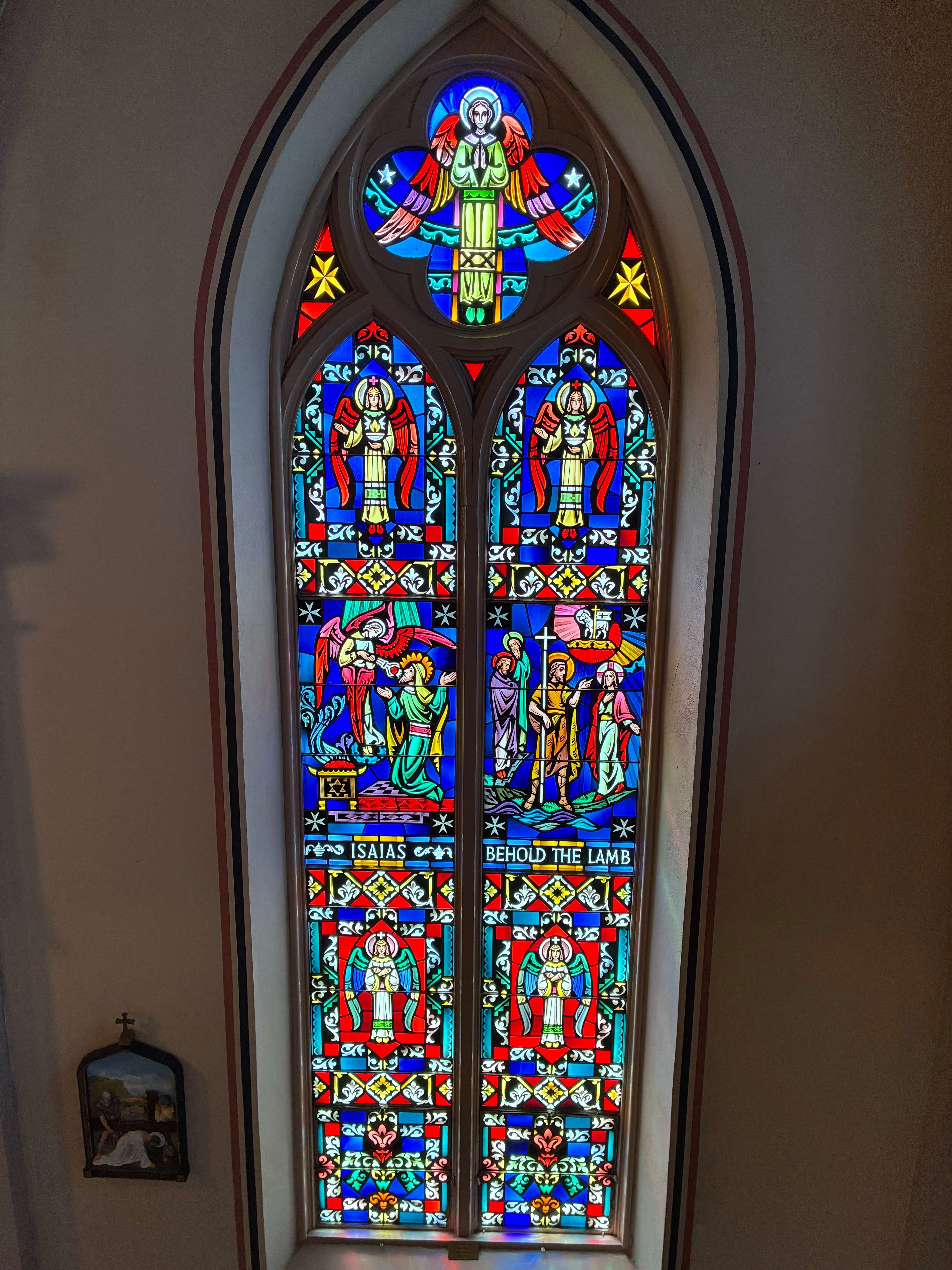 A stained-glass window depicts the prophet Isaiah, left, and a biblical scene representing “Behold the Lamb,” right, surrounded by angels and intricate religious imagery. Photo by Alin Hett/Hays Post