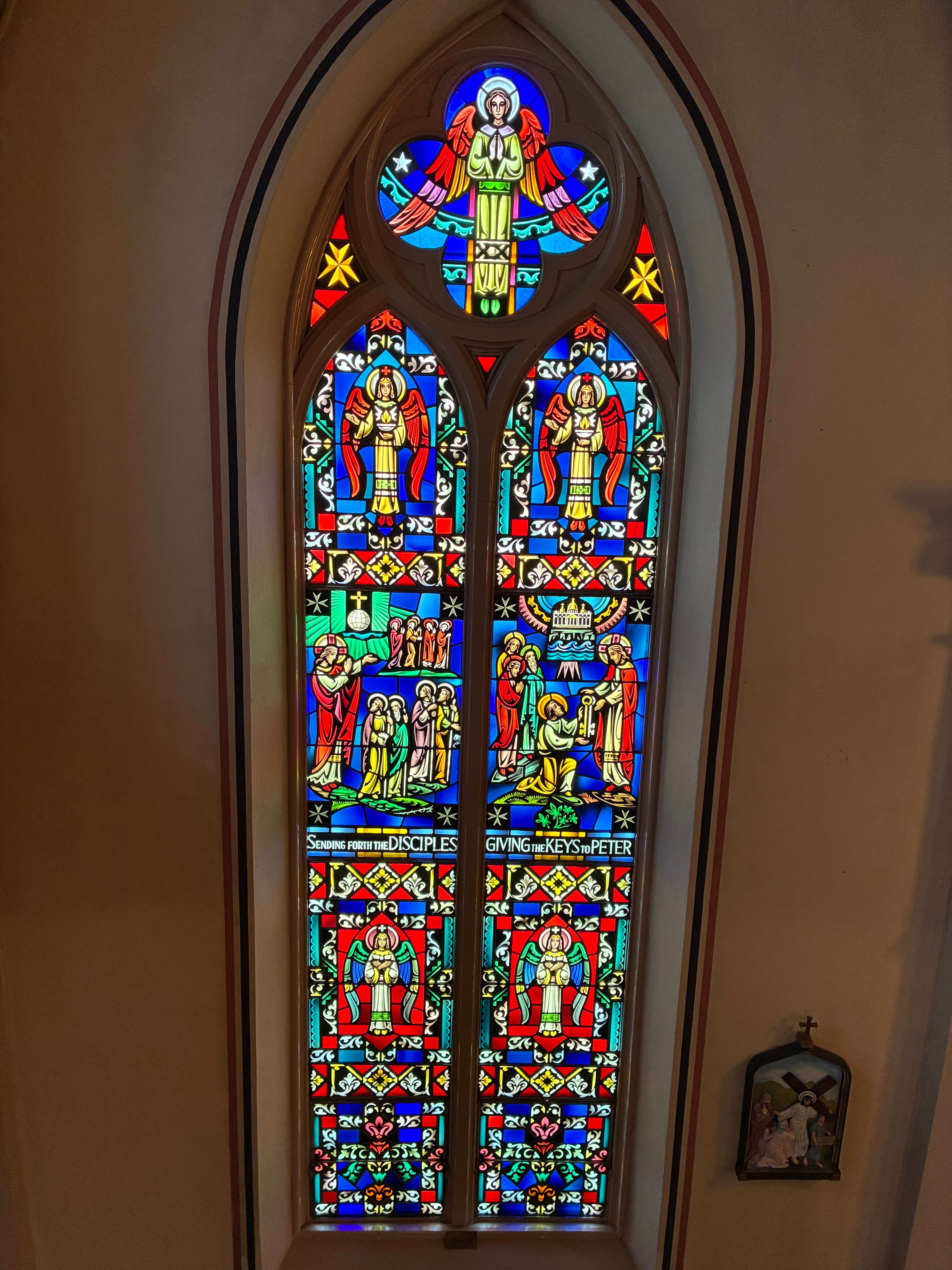 A stained-glass window depicts the biblical scenes of Jesus sending forth the disciples, left, and giving the keys to Peter, right, surrounded by angels and intricate religious imagery. Photo by Alin Hett/Hays Post