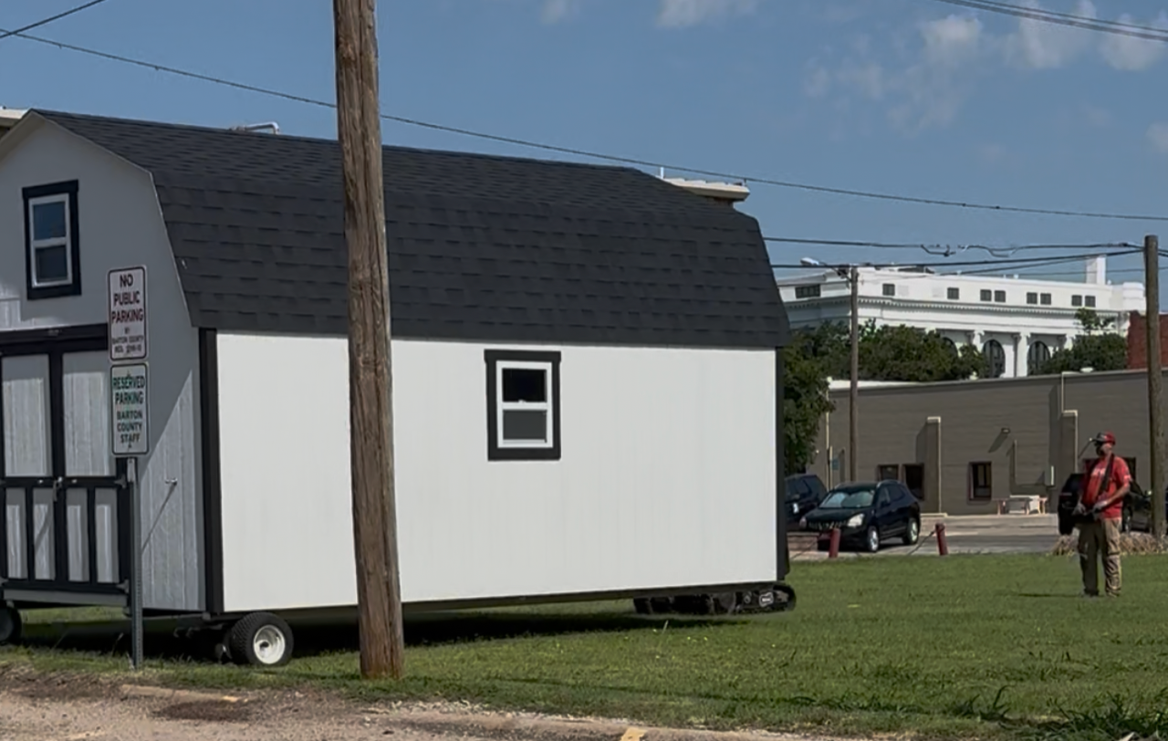 A representative of Sturdi-Bilt uses a hand-held remote to guide a storage shed into place.