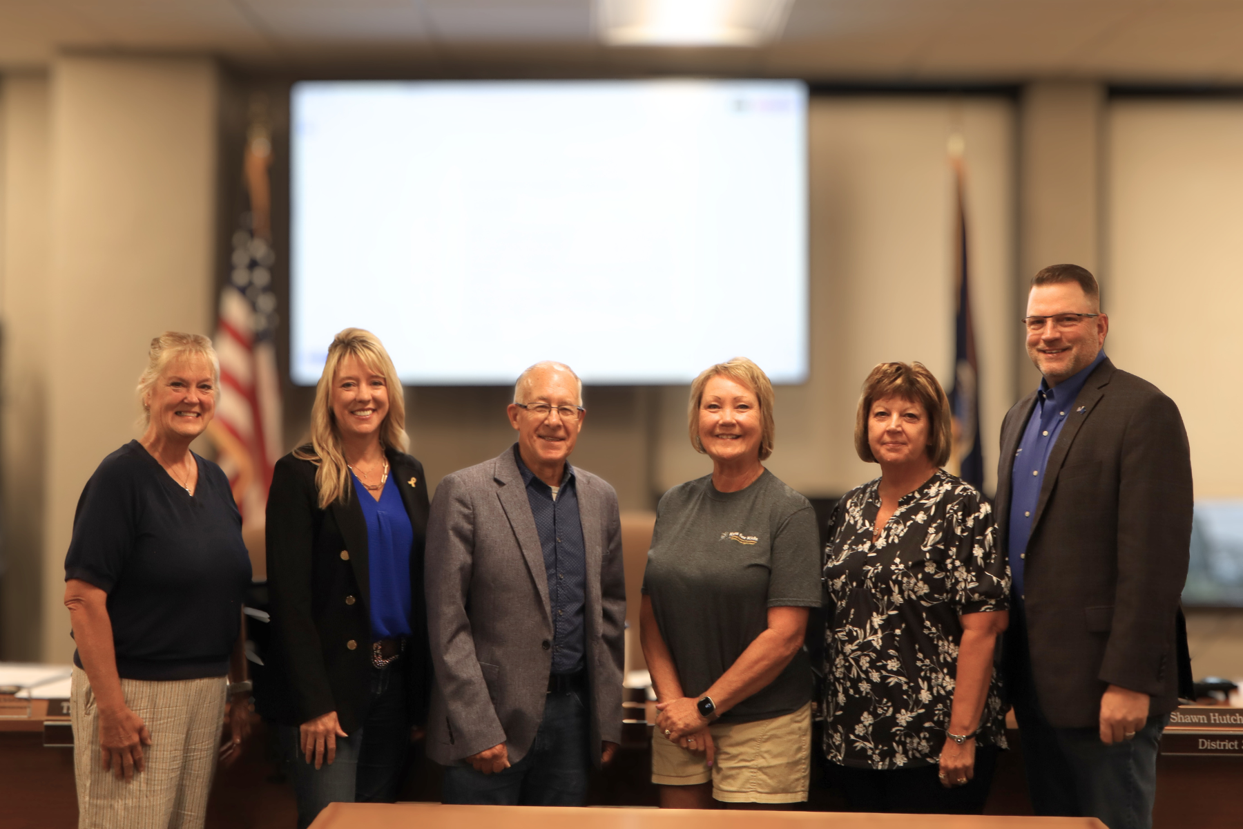 Kans for Kids Director Mary Dutton is pictured with Duane Reif, one of the founding supporters of Kans for Kids, and the Barton County Commission following the adoption of Proclamation 2026-11.